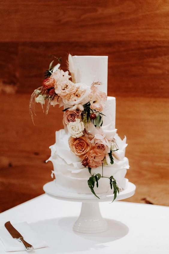white wedding cake dotted with blush and orange flower decoration for april wedding color schemes for 2023 white blush and orange
